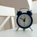 Classic blue alarm clock on a desk with houseplant in minimal setting.